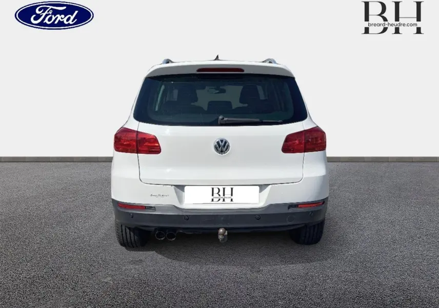 Vue arrière d'un Volkswagen Tiguan blanc Candy de 2013 avec attelage et feux arrière rouges sur sol gris.