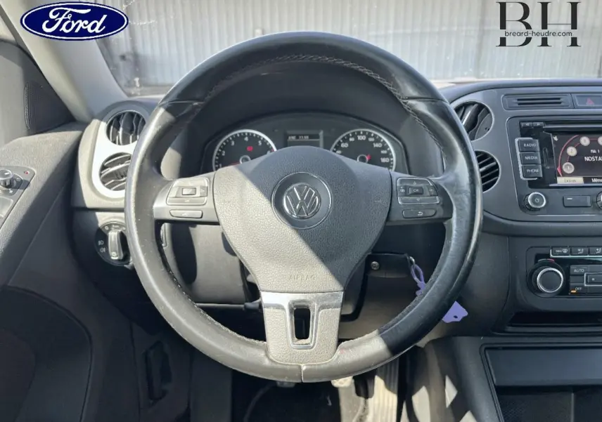 Vue intérieure centrée sur le volant cuir Volkswagen avec tableau de bord et écran tactile visibles.
