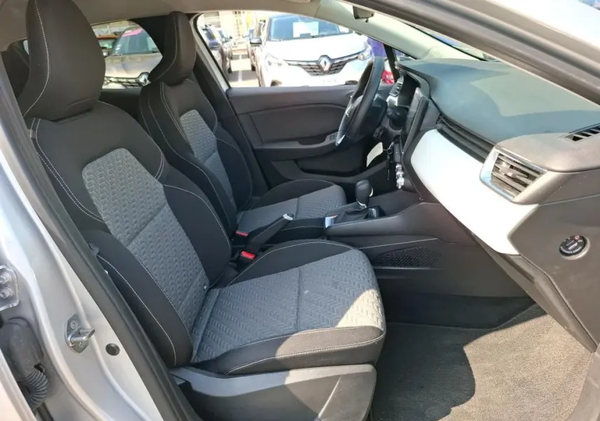 Vue intérieure côté conducteur de la Renault Clio gris platine 2023, sièges tissu bicolore et tableau de bord clair.