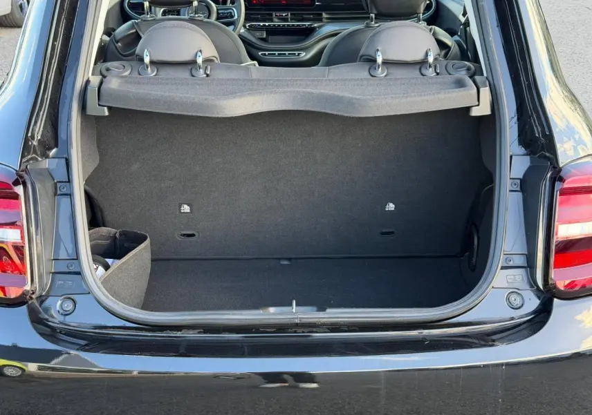 Coffre ouvert vu de l'arrière d'une Fiat 500 électrique 2024 Onyx Black pastel avec intérieur noir et tablette cache-bagages.