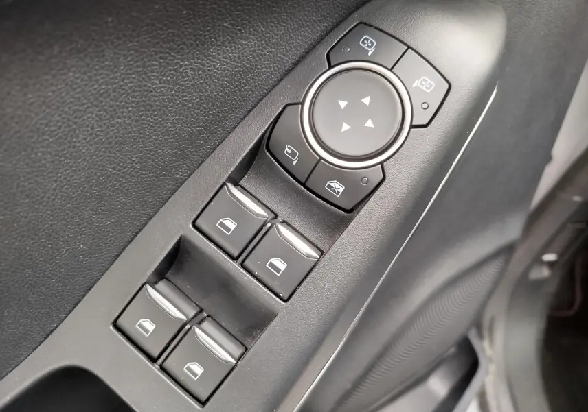 Gros plan sur les commandes de lève-vitres et réglage des rétroviseurs côté conducteur d'un Ford Puma gris 2021.