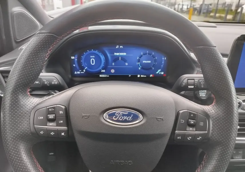 Vue rapprochée du volant perforé avec surpiqûres rouges et tableau de bord numérique du Ford Puma gris 2021.