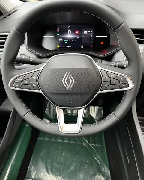 Vue rapprochée du volant cuir synthétique de la Renault Clio 2025 avec commandes multifonctions et combiné d'instruments numérique.