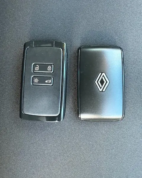 Gros plan sur deux clés noires Renault, l'une avec boutons de verrouillage et l'autre avec logo chromé, posées sur fond sombre.