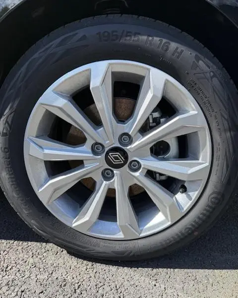 Gros plan sur la roue avant gauche d’une Renault Clio noire, mettant en valeur la jante alliage argentée au design moderne.