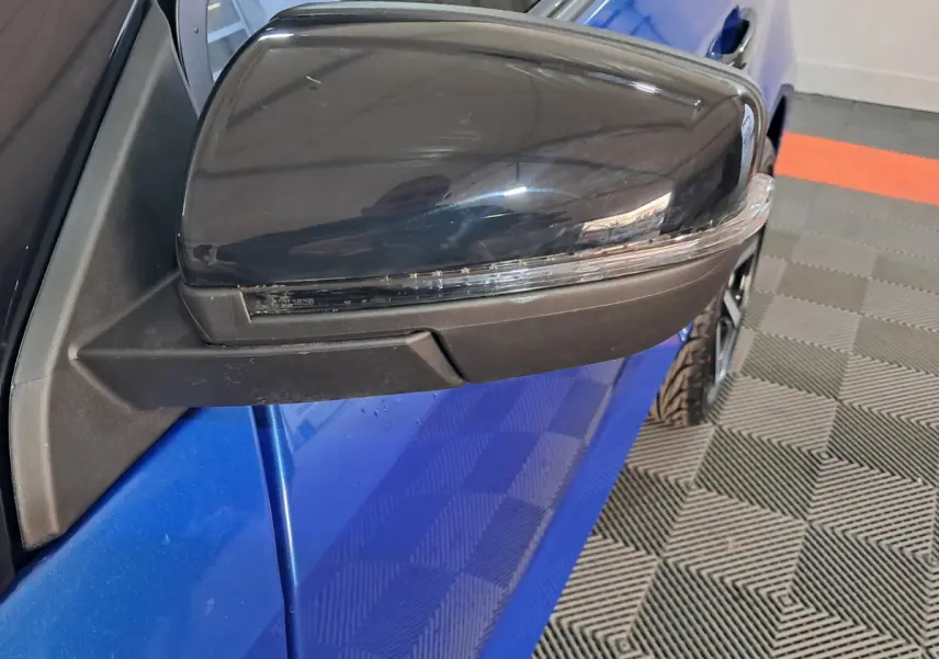 Gros plan sur le rétroviseur extérieur côté conducteur noir avec caméra, sur une Aixam Ambition bleu vue de profil.