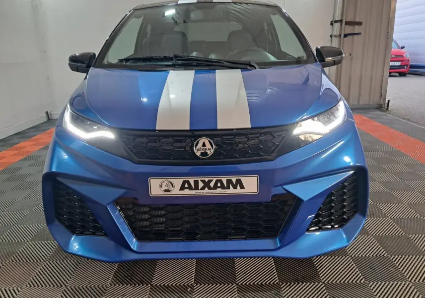 Vue frontale d'une AIXAM Ambition bleue 2026 avec bandes blanches sur le capot et phares allumés.