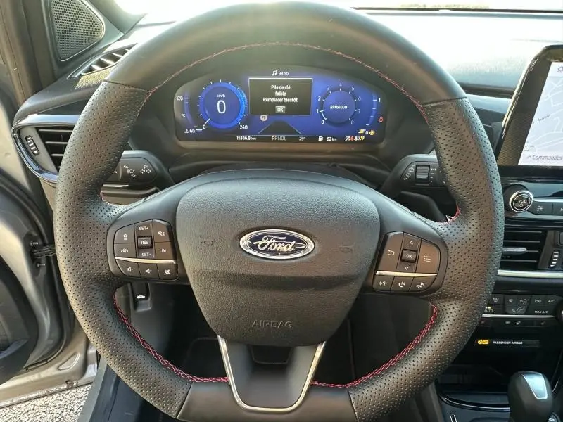 Vue centrée sur le volant perforé avec surpiqûres rouges du Ford Puma 2024, tableau de bord numérique et partie de la console centrale visible.