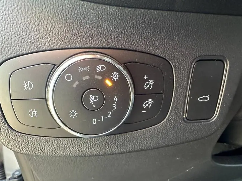 Gros plan sur la molette de réglage des phares et le bouton d'ouverture du coffre du Ford Puma 2024 gris Solar métallisé.