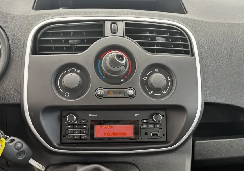 Vue rapprochée du tableau de bord central du Renault Kangoo blanc 2016, avec commandes de climatisation et radio affichant 102,40 MHz.