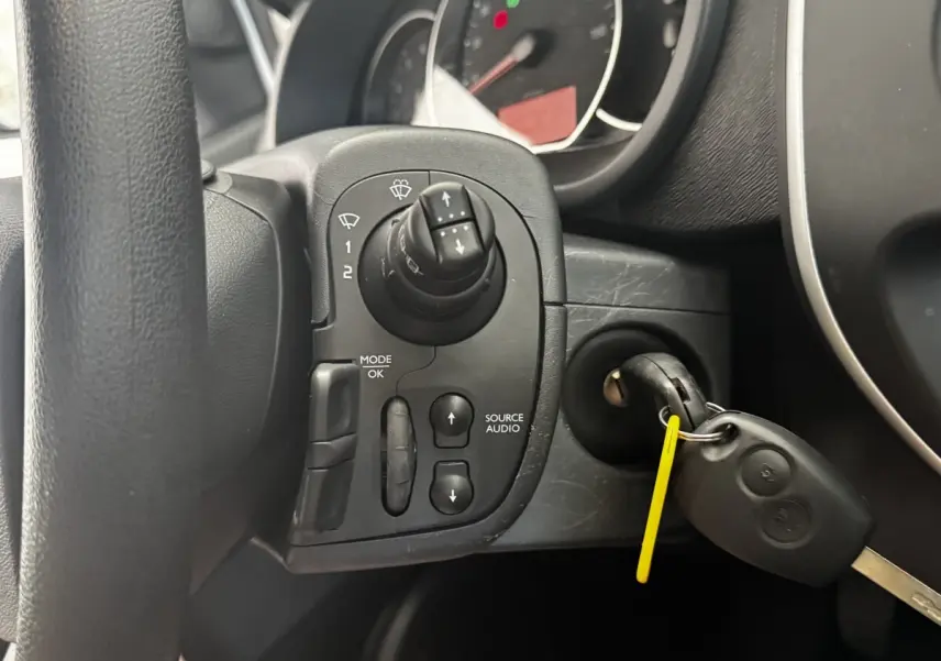 Gros plan sur la commande audio au volant et la clé insérée dans le contact d’un Renault Kangoo Zen blanc de 2016.