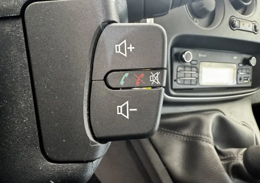 Gros plan sur les commandes au volant noir du Renault Kangoo blanc, avec la console radio en arrière-plan.