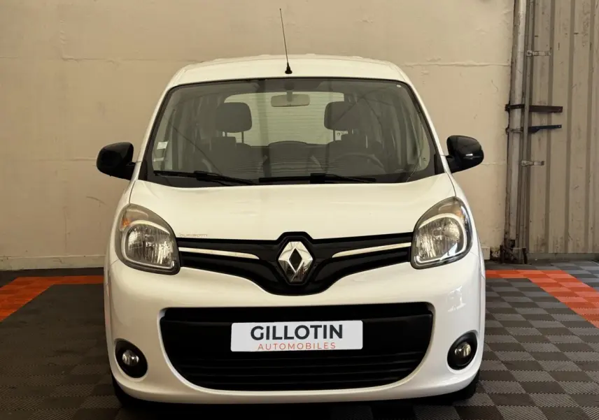 Vue avant d'un Renault Kangoo blanc avec calandre noire et phares arrondis dans un garage.