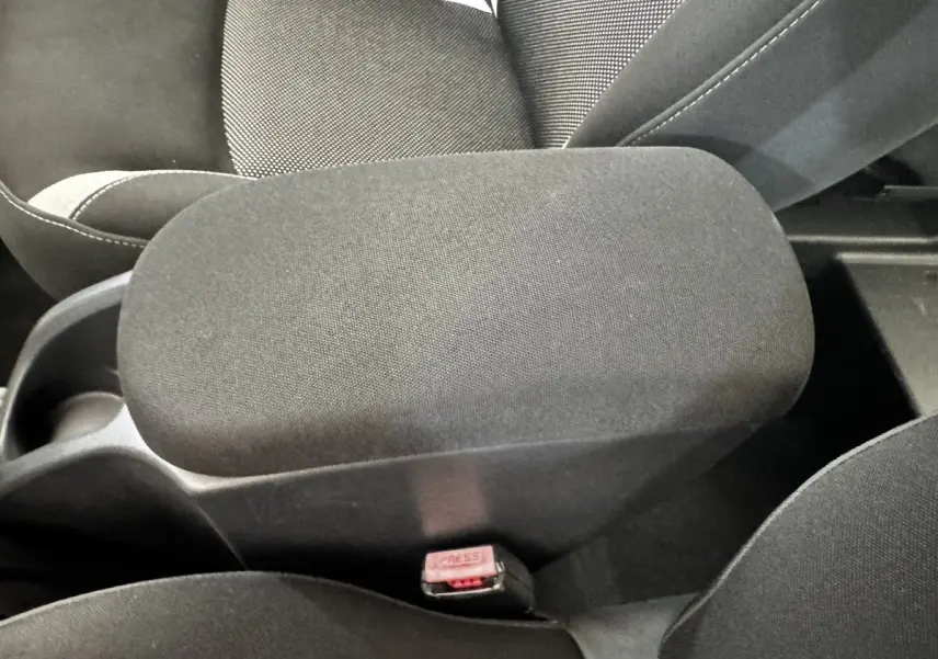 Gros plan intérieur sur l'accoudoir central noir entre les sièges avant du Renault Kangoo Zen blanc de 2016.