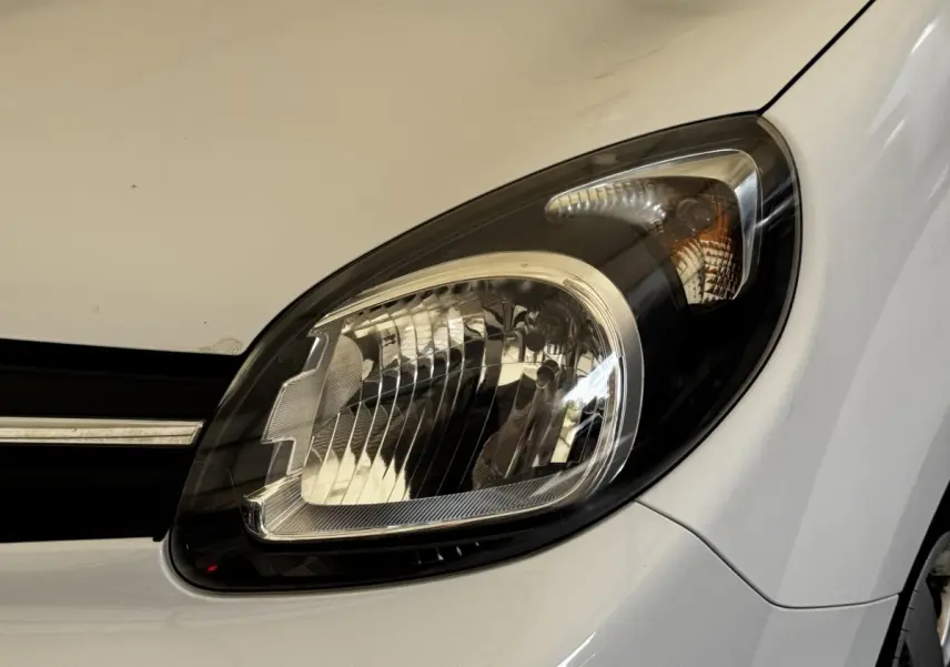 Gros plan sur le phare avant droit du Renault Kangoo blanc, mettant en valeur les détails du bloc optique.