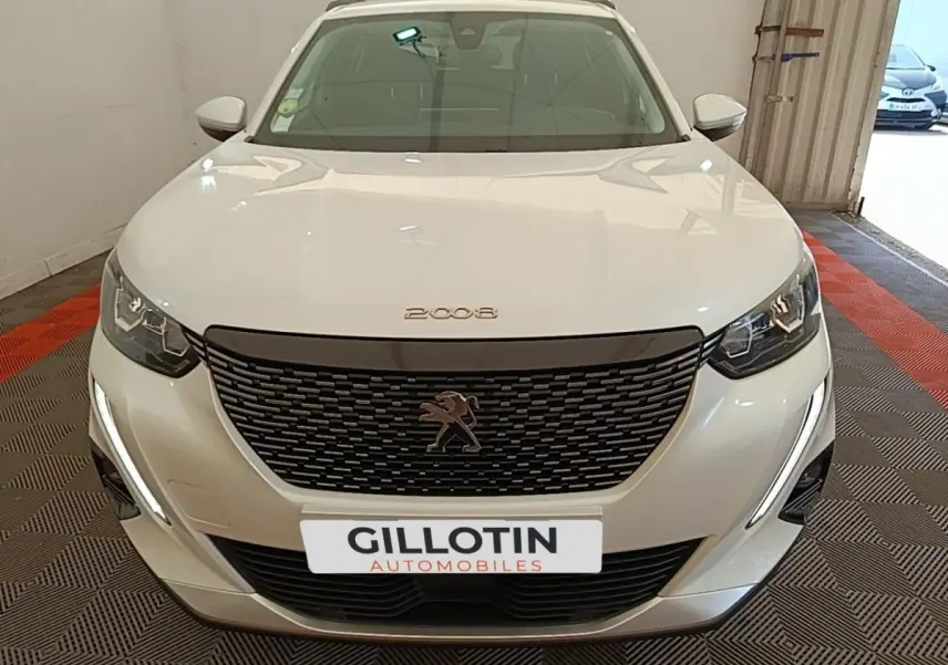 Vue avant d'une Peugeot 2008 blanche avec calandre noire et feux LED en intérieur de garage.