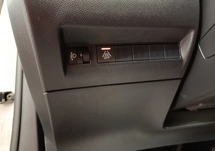Détail des commandes côté gauche sous le tableau de bord d’un Peugeot 2008 blanc, bouton d’aide à la conduite activé.