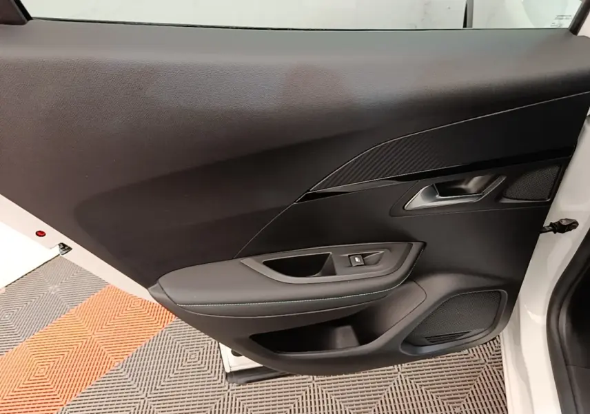 Vue intérieure côté gauche de la porte avant d'une Peugeot 2008 blanche avec garniture noire et commande de fenêtre.