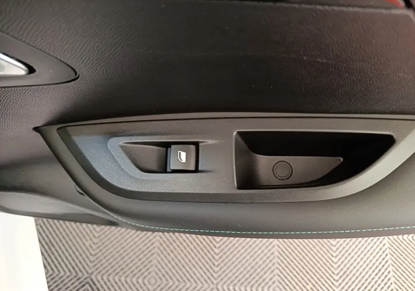 Gros plan sur la commande de lève-vitre côté conducteur du Peugeot 2008 blanc, avec surpiqûres bleues visibles.