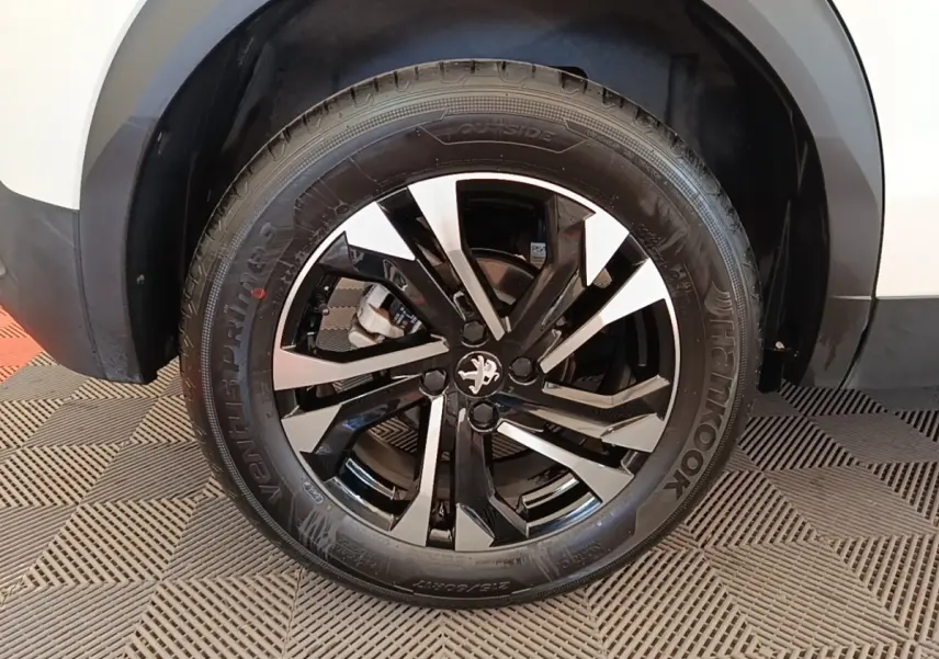 Gros plan sur la roue avant droite du Peugeot 2008 blanc, avec jante alliage noire et argentée au design moderne.