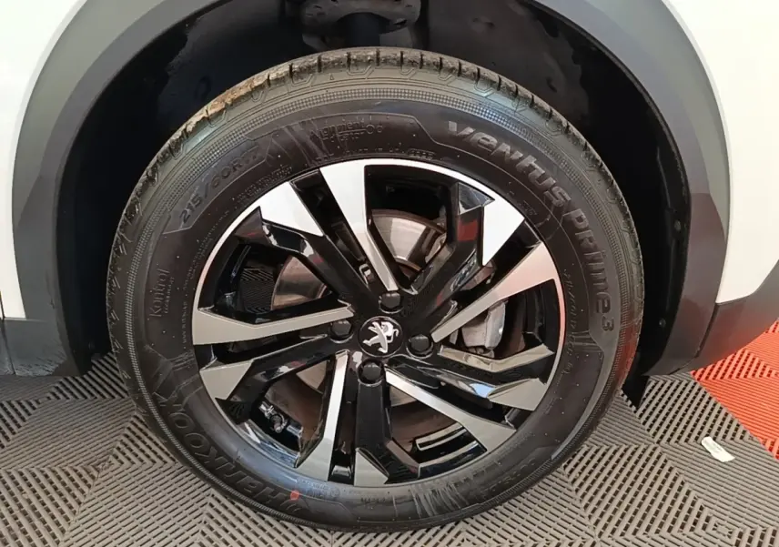 Gros plan sur la roue avant droite d’un Peugeot 2008 blanc avec jante alliage noire et argentée.