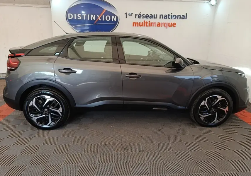 Profil droit d'une Citroën C4 gris clair 2021 avec jantes noires et toit plongeant dans un showroom.