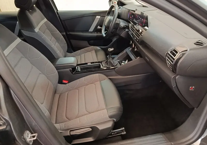 Vue intérieure côté conducteur de la Citroën C4 gris clair, avec sièges tissu et cuir, volant multifonctions et tableau de bord numérique.