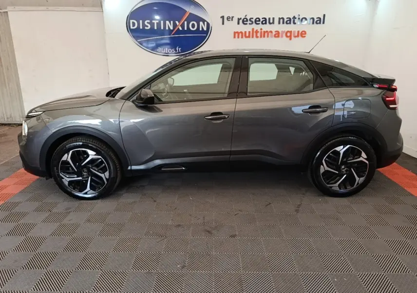 Profil côté gauche d'une Citroën C4 gris clair 2021 avec jantes noires et toit noir, en intérieur showroom.