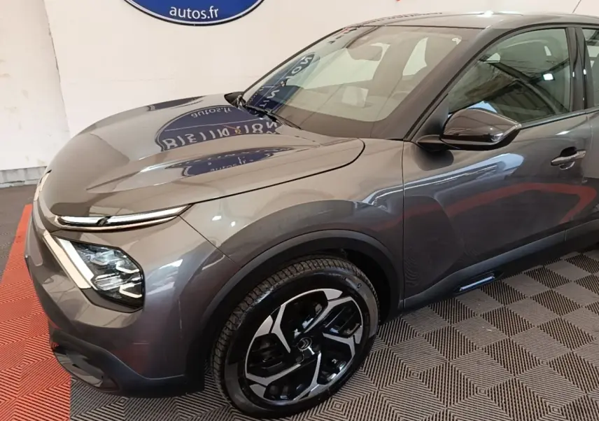 Vue 3/4 avant droit d'une Citroën C4 gris clair avec jantes noires et détails modernes au showroom.