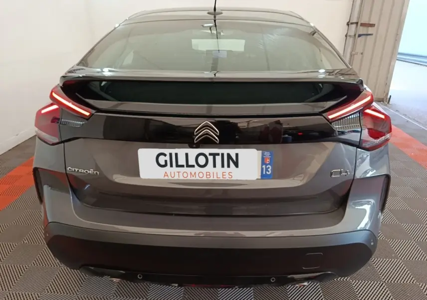 Vue arrière d'une Citroën C4 gris clair 2021 avec feux LED et spoiler de coffre en intérieur showroom.