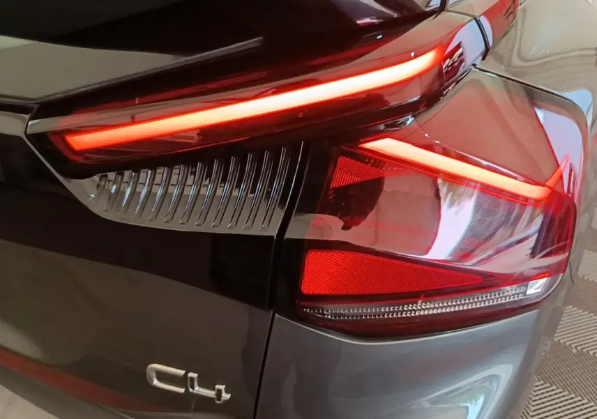 Gros plan sur le feu arrière droit rouge allumé d'une Citroën C4 gris clair, avec logo C4 visible sur la carrosserie.