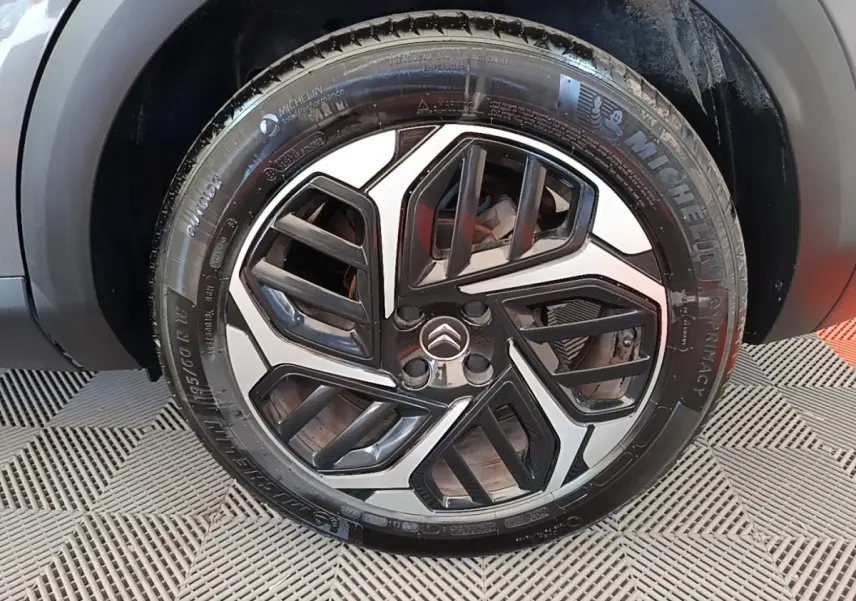 Gros plan sur la roue avant droite d’une Citroën C4 gris clair avec jante alliage au design géométrique noir et argent.