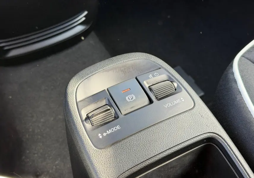 Gros plan sur la console centrale avec commandes e-MODE et volume, siège tissu noir monogramme Fiat visible à droite.