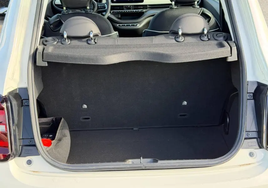 Coffre ouvert vu de l'arrière d'une FIAT 500 e 118ch Ice White pastel, montrant l'intérieur noir et tablette cache-bagages.