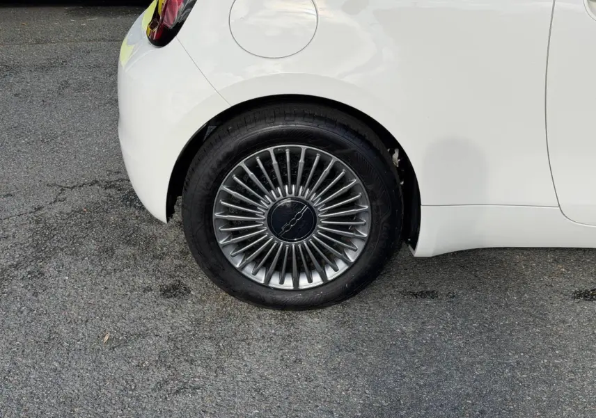 Gros plan sur la roue arrière droite d'une Fiat 500 e 118ch MY24 Ice White pastel avec jante à rayons fins.