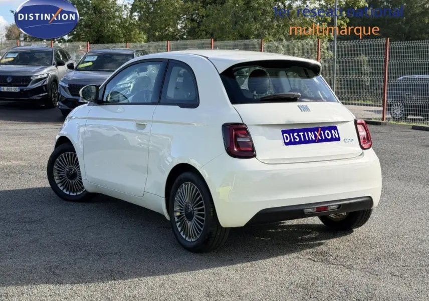 Vue 3/4 arrière droite de la Fiat 500 électrique 2024 en Ice White pastel avec jantes spécifiques et becquet noir.