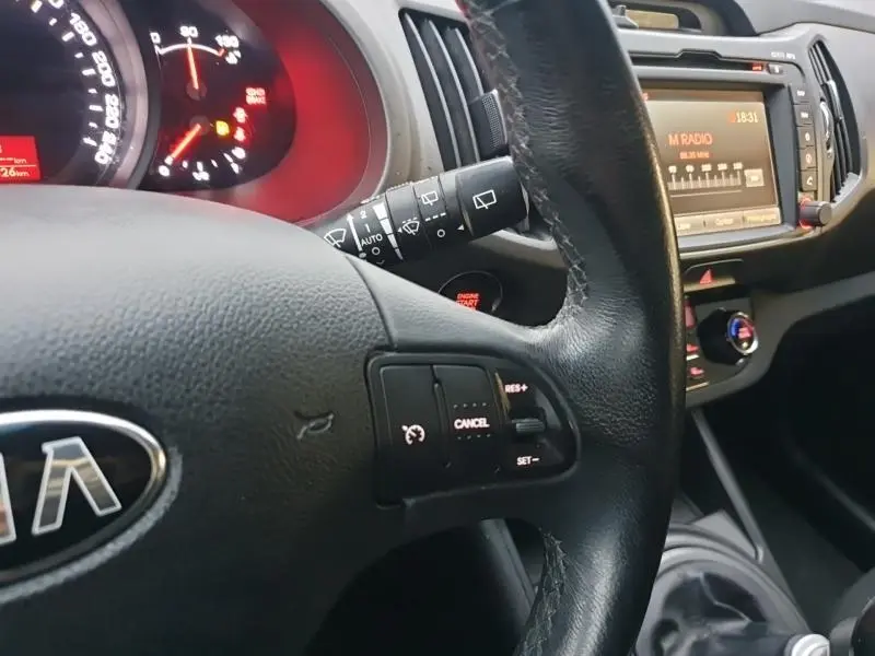 Intérieur du Kia Sportage 2013, vue rapprochée du volant cuir multifonction et tableau de bord avec écran central allumé.