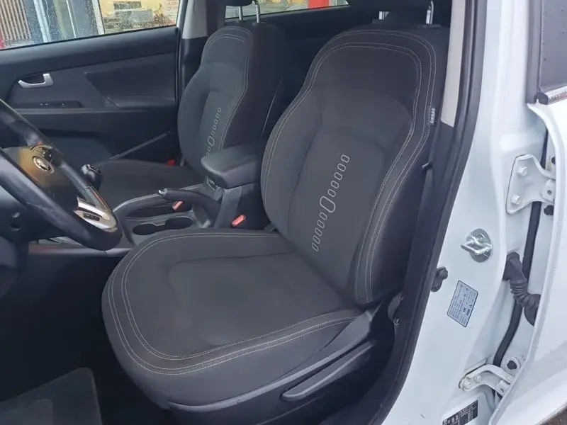 Intérieur avant droit du KIA SPORTAGE blanc 2013, sièges tissu noirs avec coutures contrastées et accoudoir central.