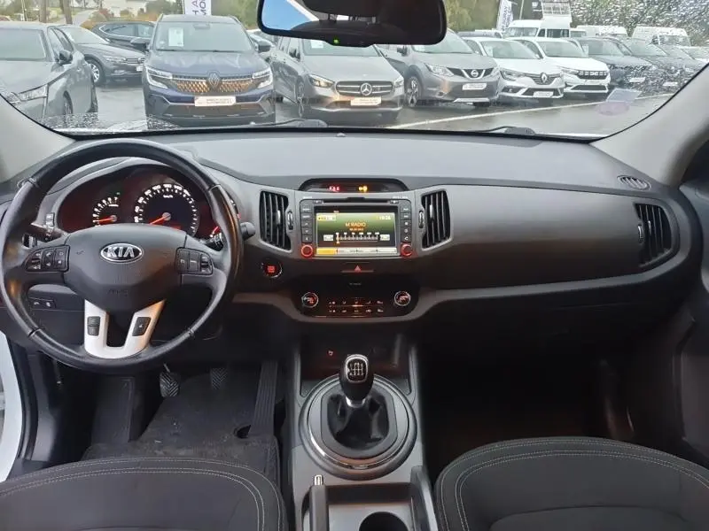 Tableau de bord et volant cuir noir du Kia Sportage 2013, avec écran central et levier de vitesse manuel visible.
