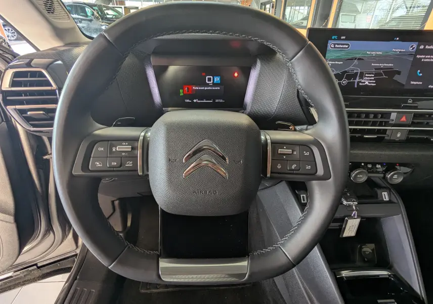 Vue centrée sur le volant noir du Citroën C4 2024 avec tableau de bord numérique et écran tactile GPS.