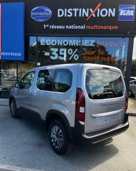 Vue 3/4 arrière droite d'un Peugeot Rifter gris foncé 2024 stationné devant une vitrine avec enseigne Distinxion.
