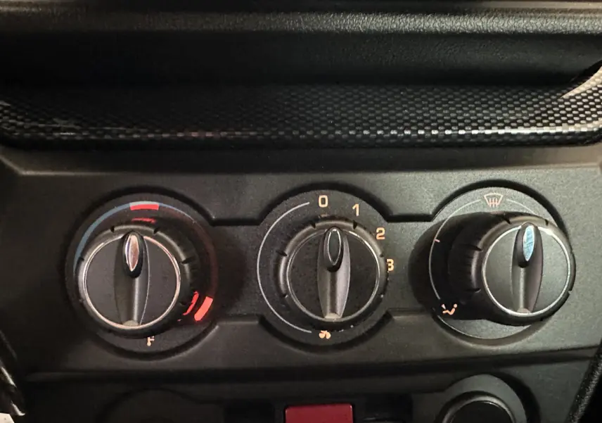 Gros plan sur les commandes de climatisation noires de l'AIXAM Ambition rouge, avec réglages de température, ventilation et désembuage.