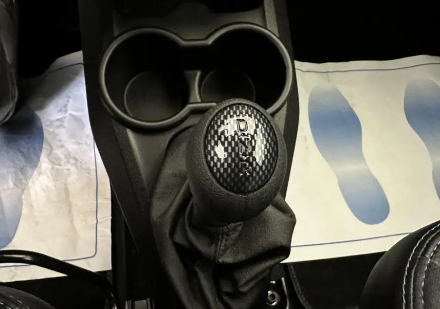 Gros plan sur le levier de vitesses automatique noir avec marquage D, N, R, T dans l'habitacle d'une Aixam rouge.