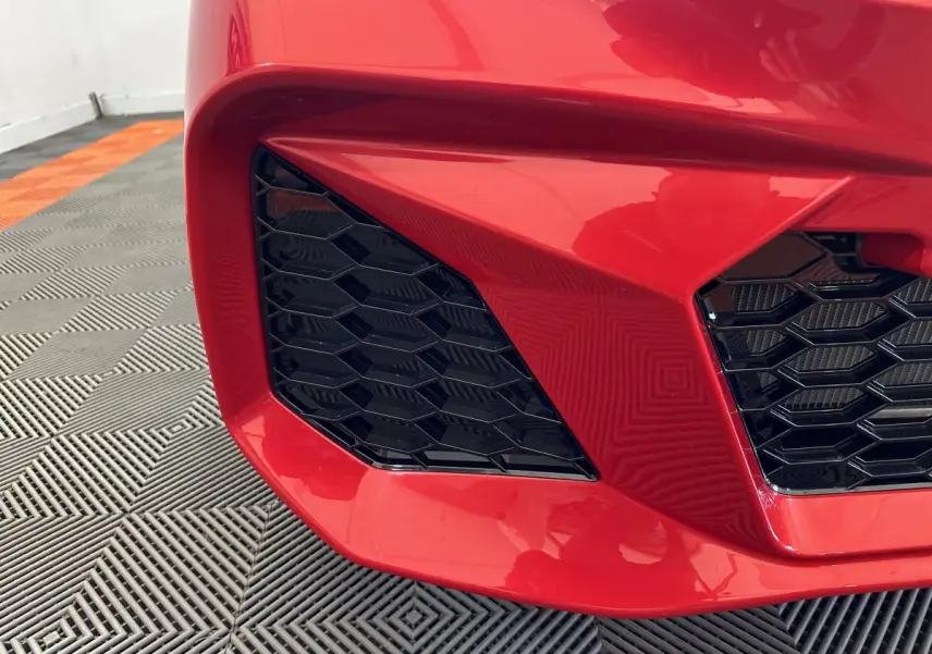 Gros plan sur la calandre avant gauche rouge de l'AIXAM AMBITION 0.5 CITY COUPE GTI E5+ avec grille noire hexagonale.