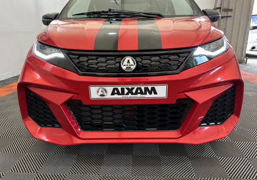 Vue frontale rapprochée de l'AIXAM AMBITION rouge 2026 avec bandes noires et calandre hexagonale distinctive.