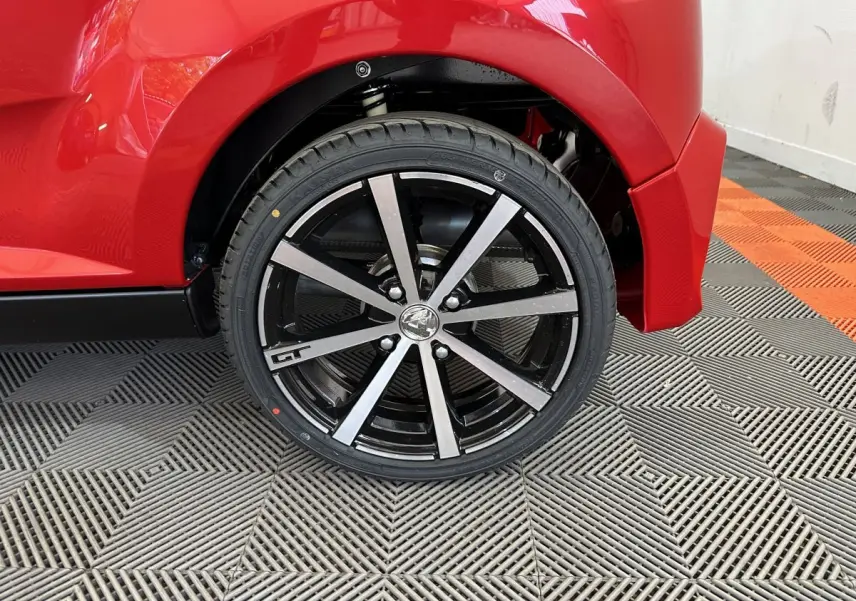 Gros plan sur la roue arrière droite de l'AIXAM AMBITION rouge 2026 avec jante GT et carrosserie brillante.