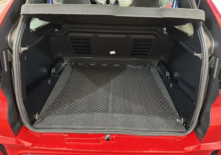 Vue arrière du coffre ouvert d'une Aixam Ambition rouge 2026, avec filet de rangement et intérieur noir.