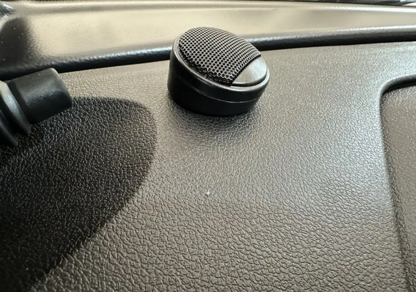 Gros plan sur un haut-parleur noir posé sur le tableau de bord texturé d'une Aixam Ambition rouge.