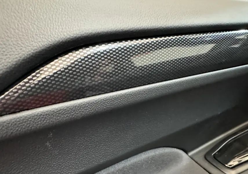 Détail intérieur montrant la garniture en carbone sur la porte côté conducteur de l'AIXAM AMBITION rouge 2026.