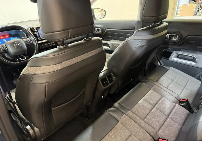Vue intérieure arrière du Citroën C5 Aircross Hybrid avec sièges bi-matière cuir et tissu gris, volant multifonctions visible.